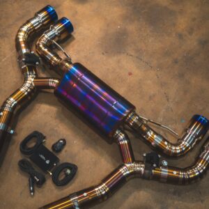 Colorful titanium exhaust pipes arranged on a concrete workshop floor, with connectors and cables nearby, forming an intricate curved layout.