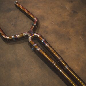 Automotive exhaust piping with multiple bends and welded joints laid on a concrete floor.