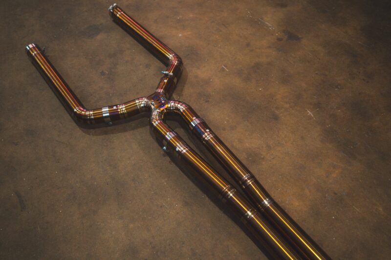 A7401073jpg - OPSHOLDERS Automotive exhaust piping with multiple bends and welded joints laid on a concrete floor.