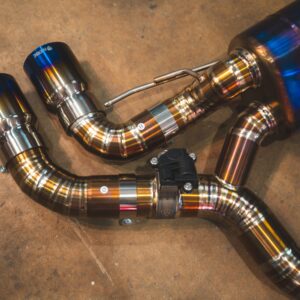 Close-up of a polished stainless steel exhaust system with curved pipes on a concrete workshop floor.