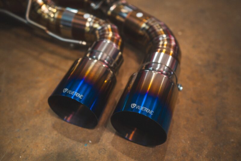 A7401076jpg - OPSHOLDERS Close-up of two metallic exhaust tips with a blue-to-orange gradient and Valvetronic branding visible on the tips.