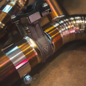 Close-up of metallic pipes and a black valve clamp, with reflective copper tubing in an industrial setting.
