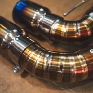 Close-up of polished stainless steel exhaust pipes curved in a circular arrangement on a workshop floor.