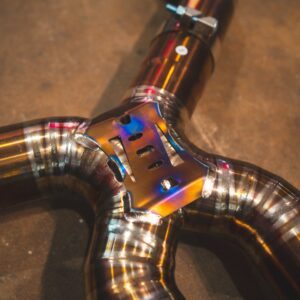 Close-up of metallic welded joints on curved chrome tubes with rainbow heat-color patina forming an intersection.