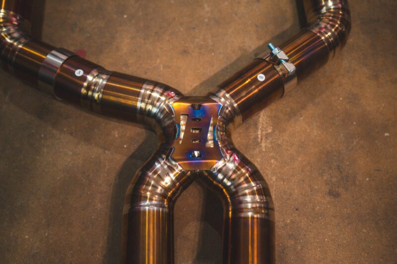 A7401081jpg - OPSHOLDERS Welded stainless steel exhaust pipes arranged in a cross on a concrete floor with clamps and a central hub.