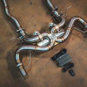 Stainless steel automotive exhaust pipes with welded bends laid out on a concrete shop floor