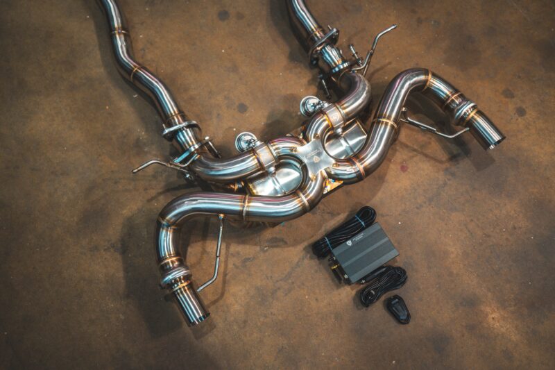Stainless steel automotive exhaust pipes with welded bends laid out on a concrete shop floor