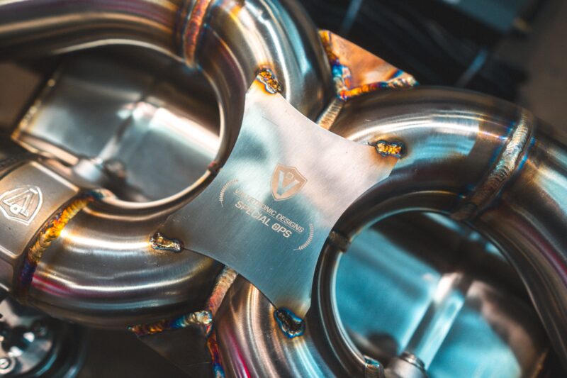 Close-up of welded stainless steel tubes with colorful heat marks in a mechanical assembly.