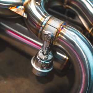 Close-up of shiny chrome motorcycle exhaust pipes with a clamp and welded joint in a workshop setting.