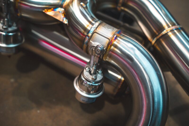 Close-up of shiny chrome motorcycle exhaust pipes with a clamp and welded joint in a workshop setting.