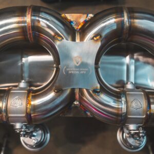 Close-up of polished stainless steel exhaust headers with welded joints and a central plaque bearing Valvetronic Designs Special OPS logo.
