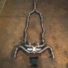 A7404834jpg - OPSHOLDERS Industrial sculpture made from welded car exhaust pipes arranged symmetrically on a brown concrete floor, resembling a humanoid frame.