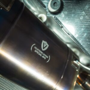 Close-up of a stainless steel exhaust pipe with Valvetronic Designs Special Ops branding, against a carbon-fiber background.