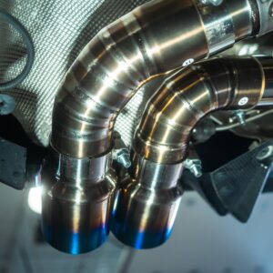 Close-up of shiny curved stainless steel exhaust pipes and clamps in a vehicle engine bay.