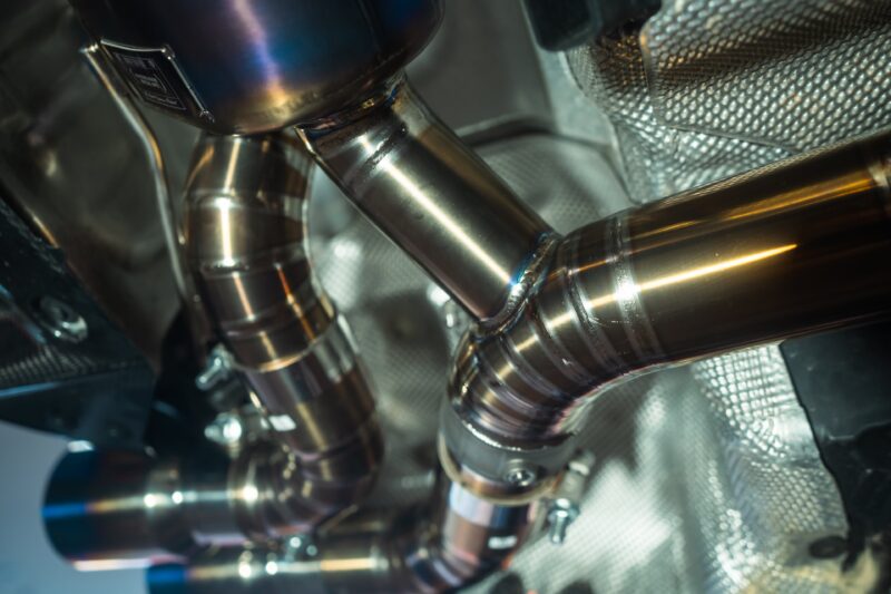 A7407925jpg - OPSHOLDERS Close-up of polished stainless steel pipes and welded joints in a metallic machine interior.