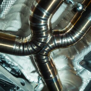 Close-up of interconnected shiny stainless steel exhaust pipes with a textured heat shield in a car's engine bay