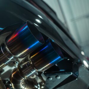 Close-up of polished chrome exhaust pipes on a dark vehicle, with blue-purple heat reflections on the metal.