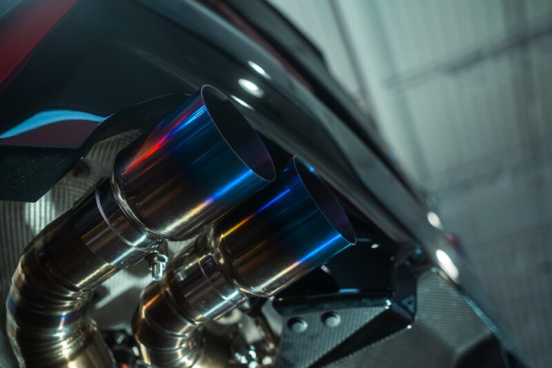 A7407938jpg - OPSHOLDERS Close-up of polished chrome exhaust pipes on a dark vehicle, with blue-purple heat reflections on the metal.