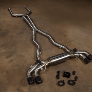 Stainless steel automotive exhaust pipes and mufflers laid out on a workshop floor with clamps and connectors visible
