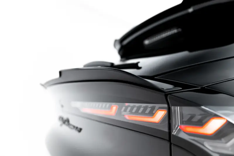 Close-up of a dark car rear with glowing red/orange taillights and sleek lines