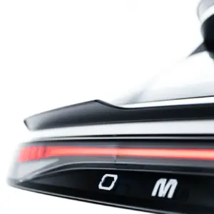 Close-up of a car's rear end, showing a bright red horizontal taillight and glossy black trim.