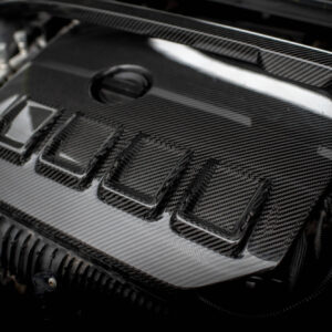 Close-up of a car engine bay with carbon fiber panels and metal components visible around it.