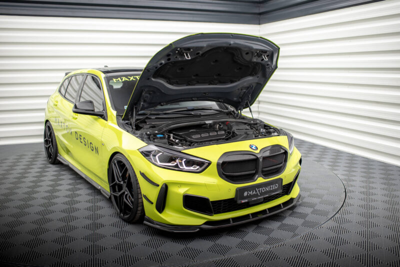 Bright lime-yellow BMW sports sedan with its hood open, exposing the engine in a showroom setting.