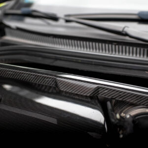 Close-up of a car engine bay with carbon fiber panels and black metal components in a sleek, glossy finish.