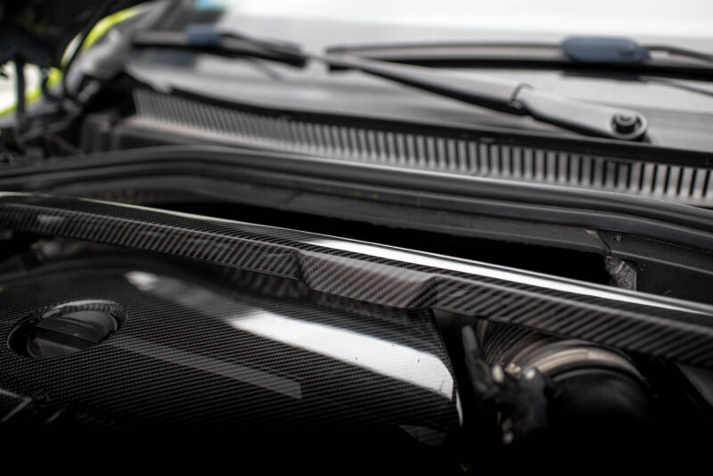 Close-up of a car engine bay with carbon fiber panels and black metal components in a sleek, glossy finish.",