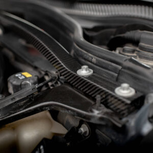 Close-up of an automotive engine bay with hoses, a coolant reservoir, and a metal bolt in focus under dim lighting.