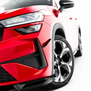 Close-up of a red car's front end showing the headlight, black grille, and alloy wheel with RS badge visible on the grille.