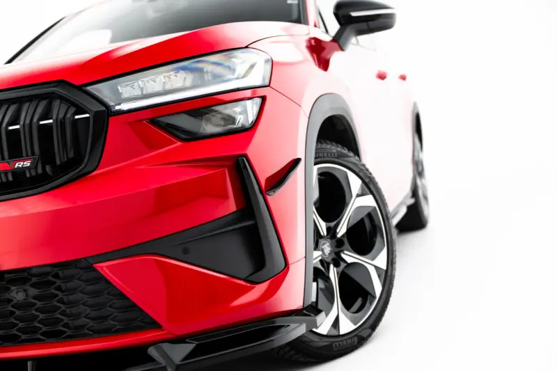 Close-up of a red car's front end showing the headlight, black grille, and alloy wheel with RS badge visible on the grille.