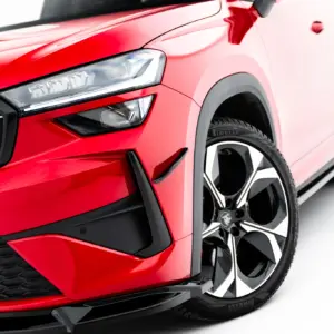 Close-up of the front left corner of a red car, highlighting the angular LED headlight, black grille, and wheel with alloy rim.