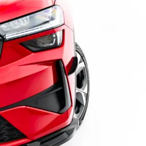 Close-up of a red car's front end, showing the headlight, grille, and lower bumper.