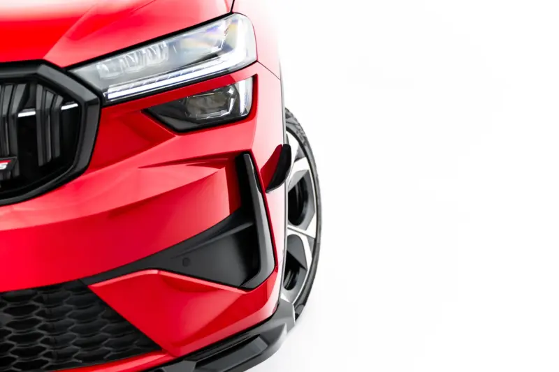 Close-up of a red car's front end, showing the headlight, grille, and lower bumper.