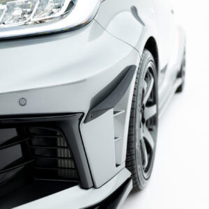 Close-up of a silver car's front left corner showing the headlight, bumper, and part of the tire and grille.