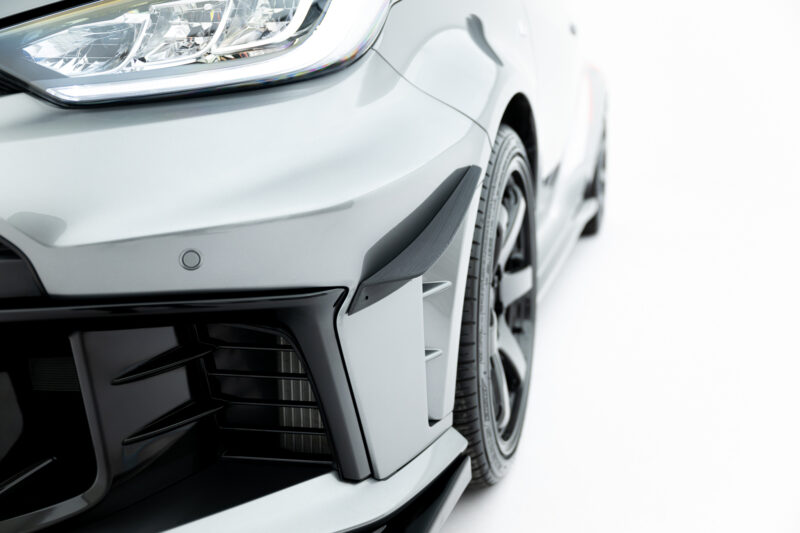 Close-up of a silver car's front left corner showing the headlight, bumper, and part of the tire and grille.