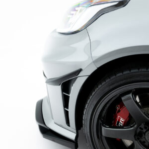 Close-up of a white car's front left corner showing the headlight and black wheel with red brake caliper behind it