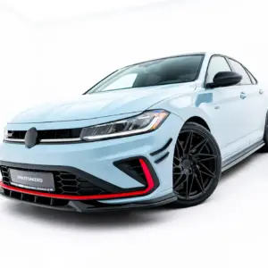 Front-left angled view of a light-blue sporty sedan with large black wheels and a black front grille showing a VW badge and red accents at the bumper edge.