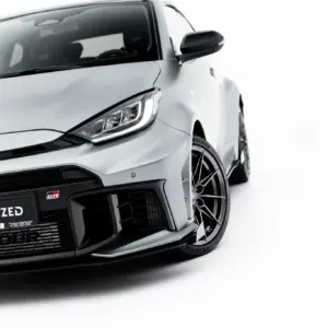 Close-up of a white Toyota front end, featuring the emblem, headlight, and black grille detailing.