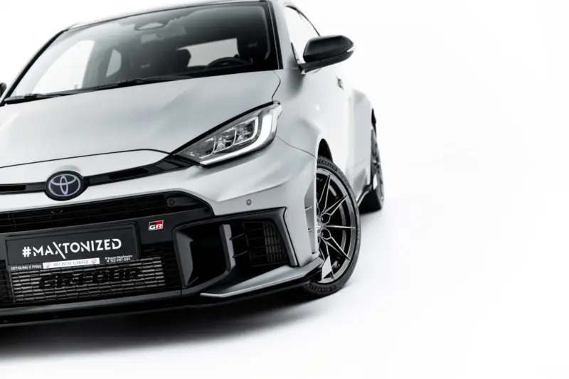 pol_po_Front-Flaps-Flaps-Toyota-GR-Yaris-Mk4-Facelift-23785_6webp - OPSHOLDERS Close-up of a white Toyota front end, featuring the emblem, headlight, and black grille detailing.