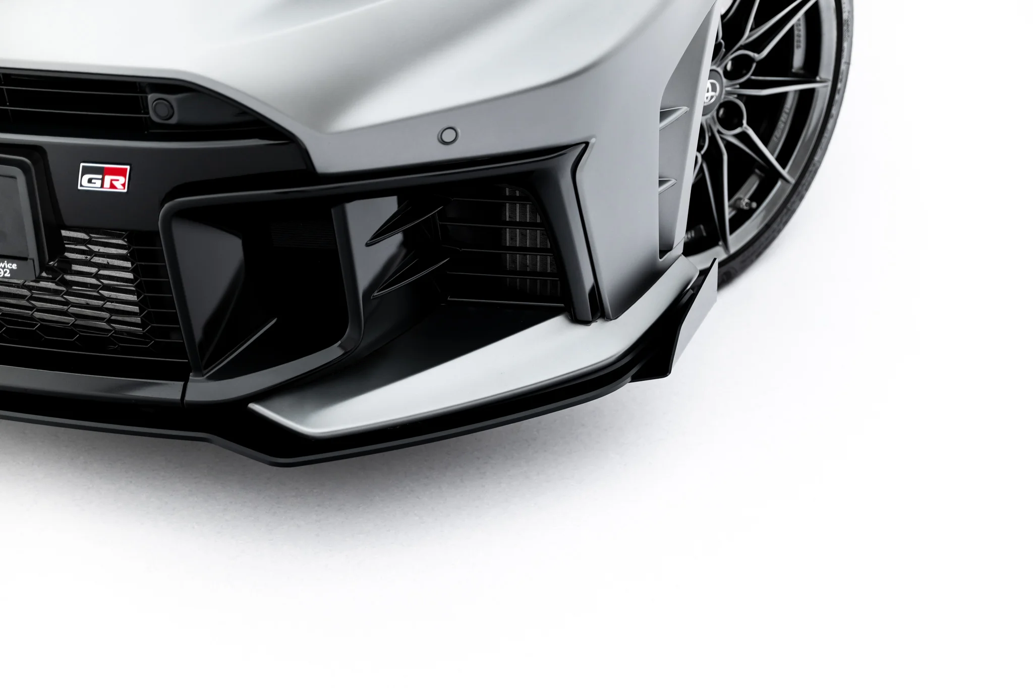 pol_po_Front-Flaps-Flaps-Toyota-GR-Yaris-Mk4-Facelift-23785_7webp - OPSHOLDERS Close-up of the front left corner of a gray sports car, showing the grille, bumper, and a visible GR badge.