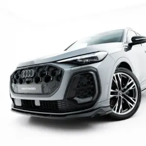 Front-right close-up of a silver Audi SUV in a studio setting, showing the bold grille, headlight, and large alloy wheel with '#MAXTONIZED' plate.