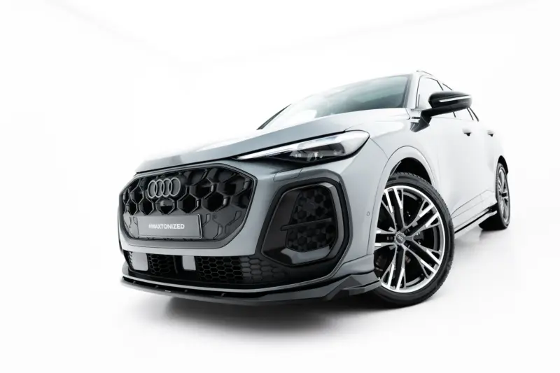 Front-right close-up of a silver Audi SUV in a studio setting, showing the bold grille, headlight, and large alloy wheel with '#MAXTONIZED' plate.