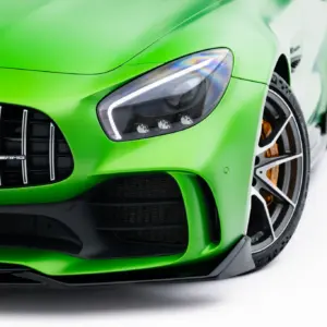 Close-up of a bright green sports car front, featuring the headlight, grille with vertical slats, and AMG badge in the center.