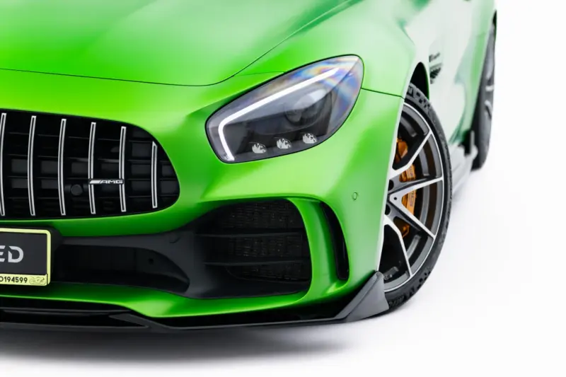 pol_po_Front-Splitter-Mercedes-AMG-GT-R-C190-Facelift-23888_1webp - OPSHOLDERS Close-up of a bright green sports car front, featuring the headlight, grille with vertical slats, and AMG badge in the center.