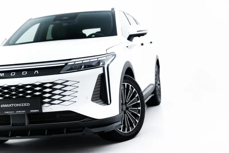 Front-left close-up of a white SUV, highlighting the bold grille, headlight, and large alloy wheel on a bright studio backdrop