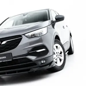 Front-left angle of a silver Opel car showing grille, headlight, and front wheel with '#MAXTONIZED' on the license plate frame.