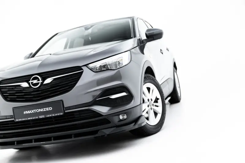 Front-left angle of a silver Opel car showing grille, headlight, and front wheel with '#MAXTONIZED' on the license plate frame.