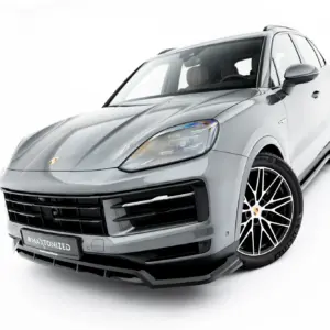 Front-left angled view of a silver Porsche SUV, highlighting the bold grille, headlight, and large multi-spoke wheels against a white background.